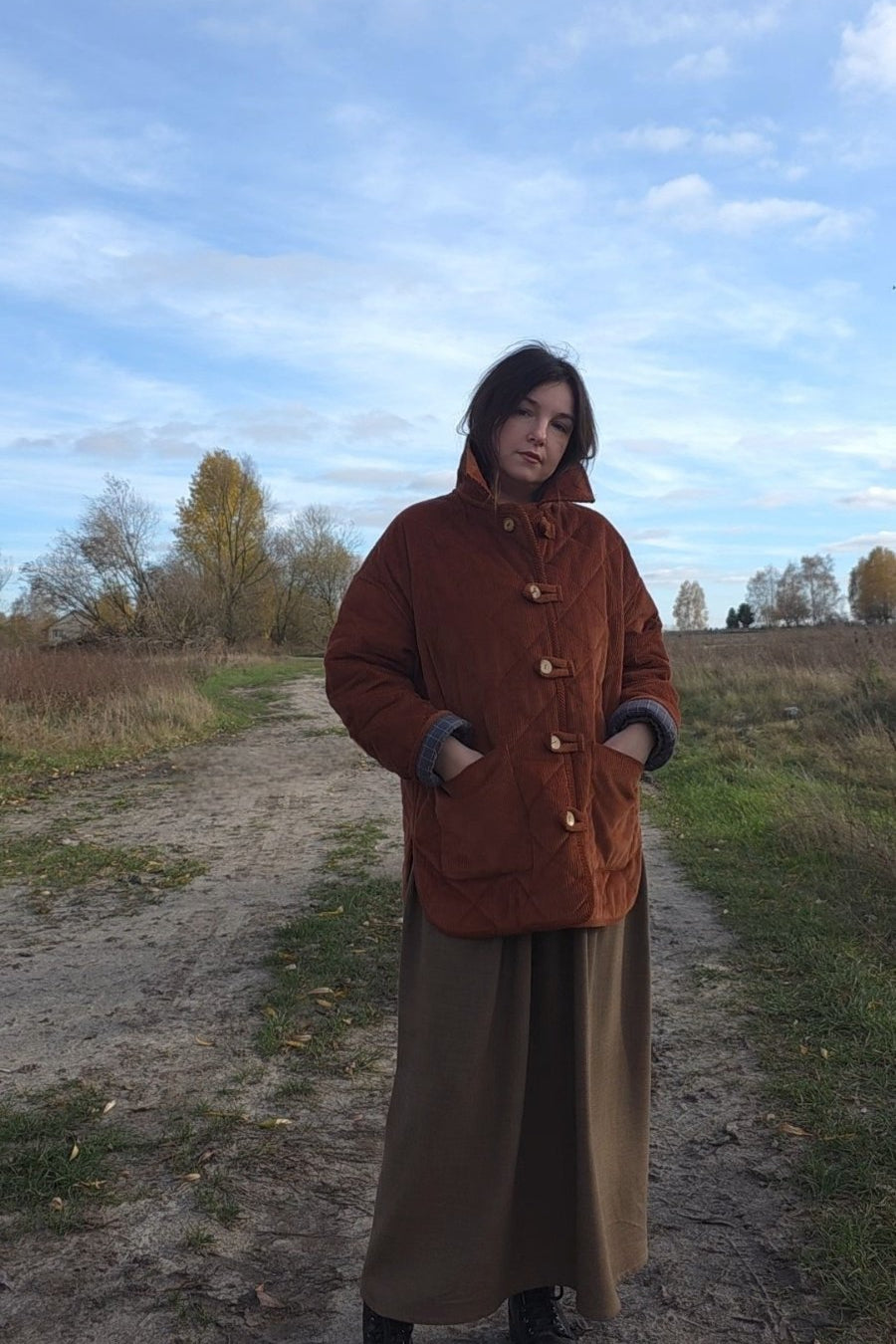 Woman wearing a rust corduroy quilted jacket with wooden buttons, styled with wide leg pants in a natural autumn setting