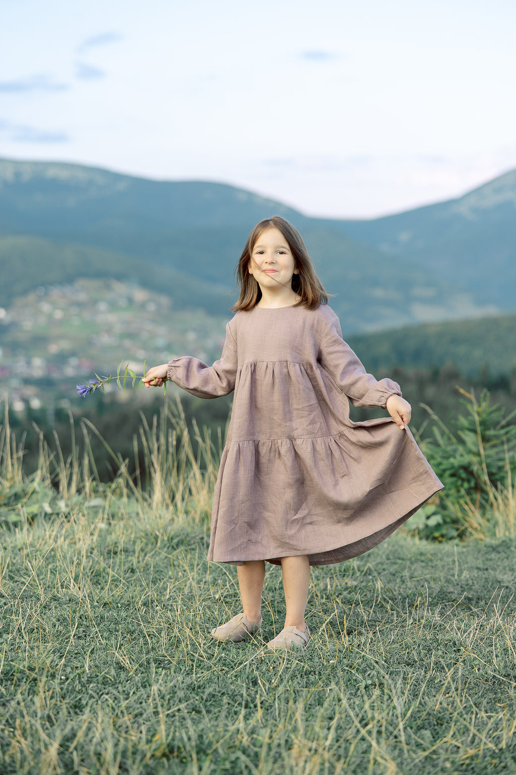 Two-tiered linen dress for little girls with long sleeves and back tie closure, displayed in pastel purple.